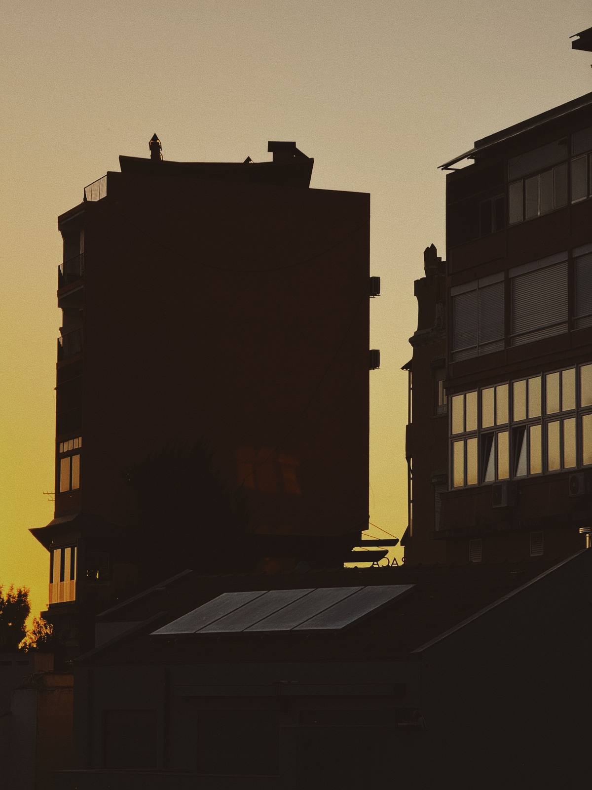 Silhouette Against Amber, Graça & Miradouros, Lisbon — Two building masses in full silhouette against a deep yellow sunset sky — bold graphic reduction, ABIASSI yellow at full saturation.