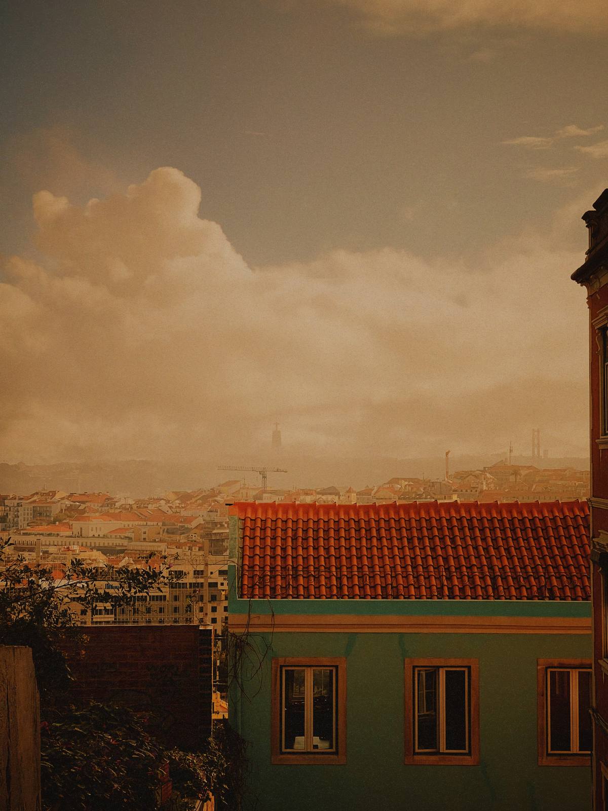 Rooftops Over the City, Graça & Miradouros, Lisbon — Warm haze over Lisbon rooftops, a teal building with red tile and ornate cornice in the foreground — the layered-city motif at its clearest.