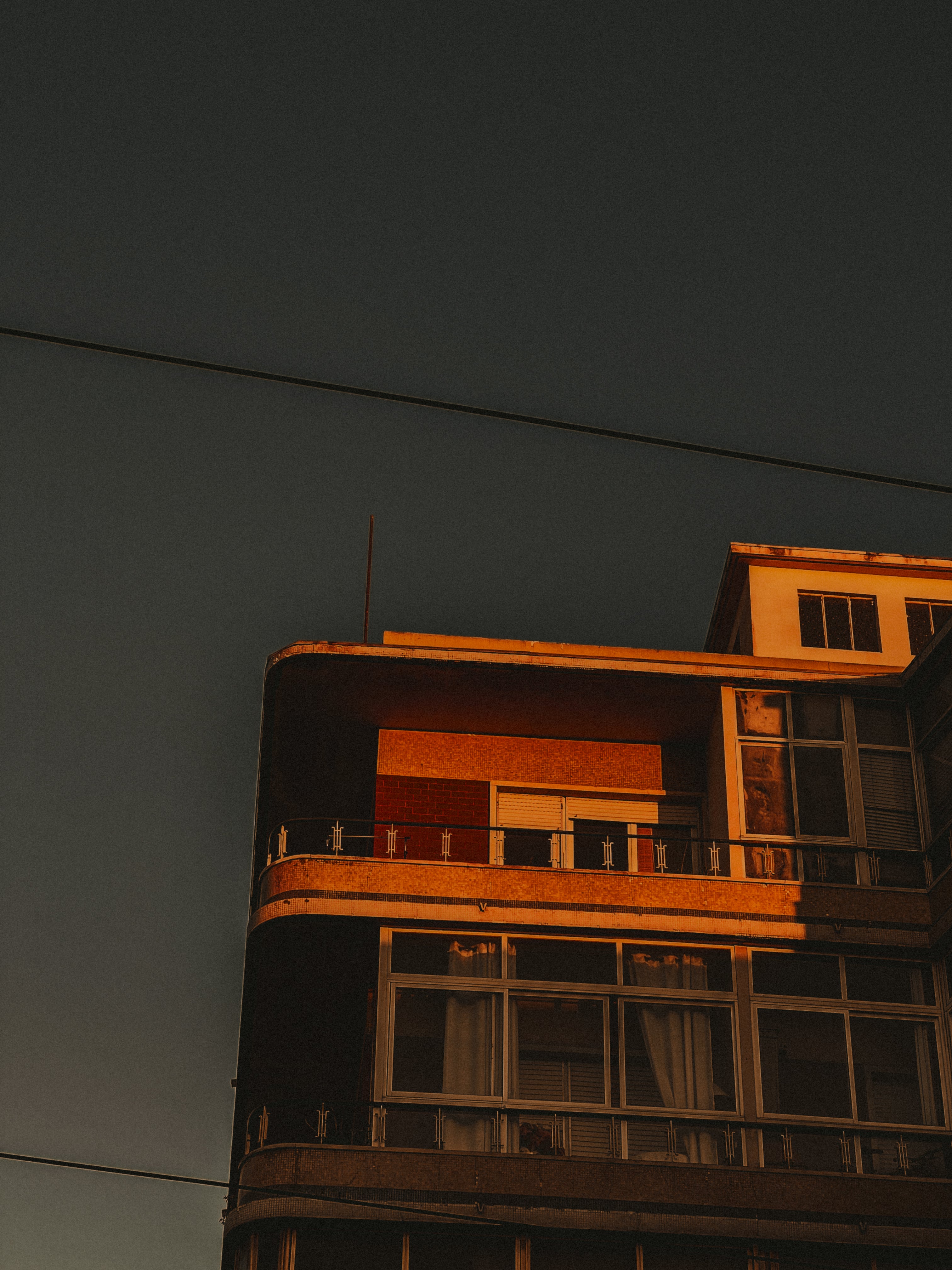 Curved balcony building from below, tram wires against teal sky — Graça, Lisbon