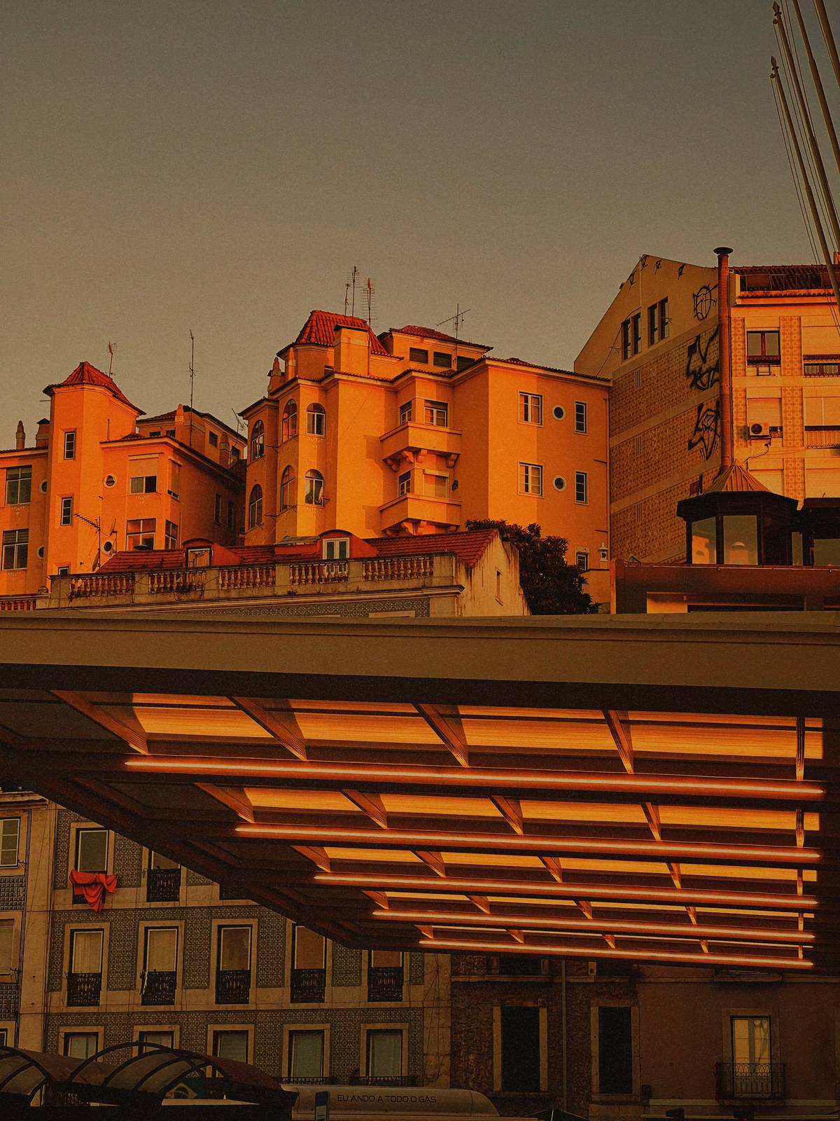 Corridor of Amber Light, Alfama, Lisbon — Deep vanishing-point corridor under a warm grid ceiling, silhouetted figures at the far end — strong perspective, brand yellow, contemplative scale.
