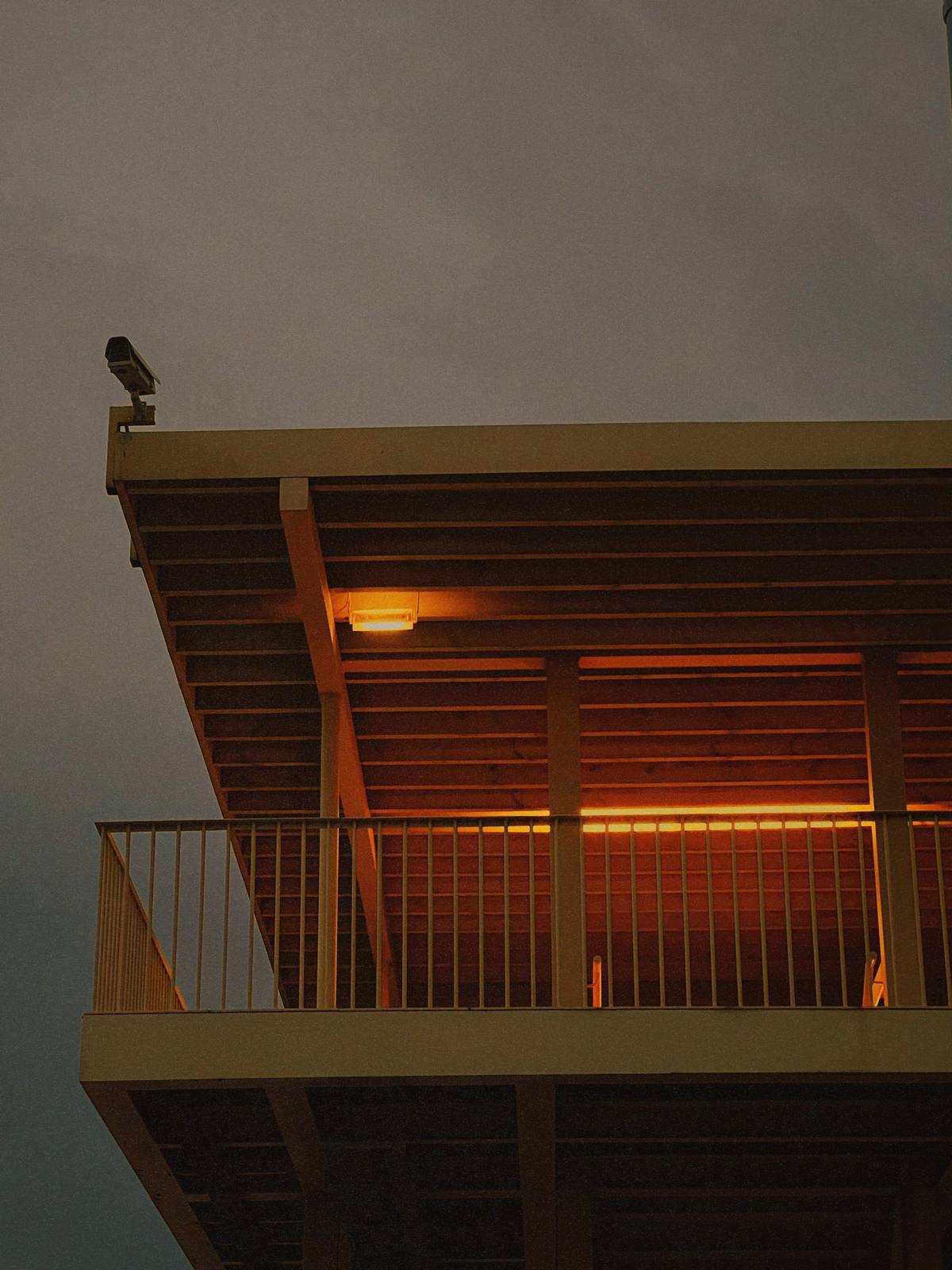Amber Under Concrete Dusk, Alfama, Lisbon — Brutalist canopy glows a deep amber against a flat grey sky — single lamp, strong geometry, bold colour tension; prints with real authority at A3.
