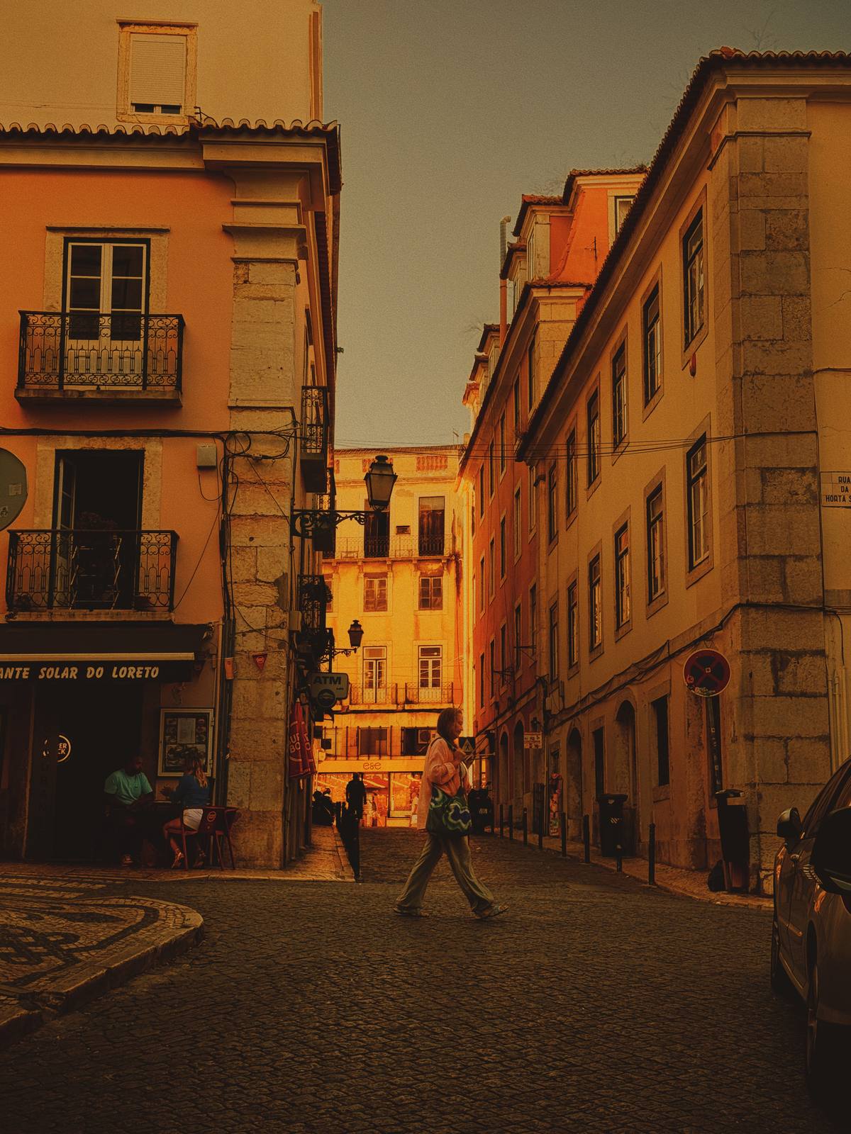 Amber Figure, Loreto, Chiado, Lisbon — Isolated figure crossing warm-lit cobblestones with architectural layers receding into golden light — textbook ABIASSI: figure in space, Lisbon amber, deliberate