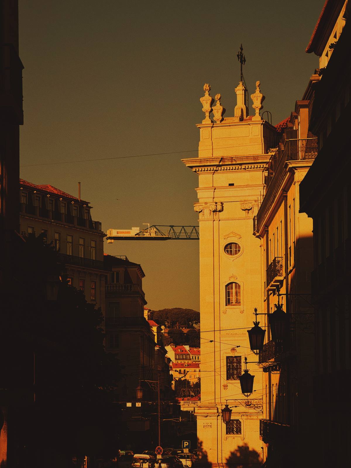 Tower Compressed in Gold, Chiado, Lisbon — Church tower emerges from deep shadow into extreme golden light with city layers behind; the telephoto compression and near-black foreground give it strong p