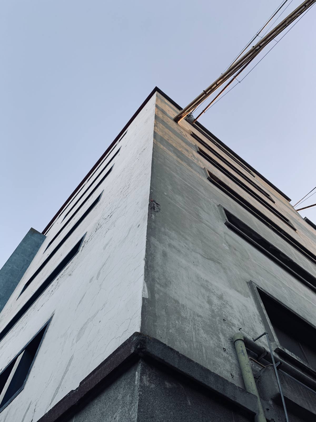 Corner Reaches The Sky, Marvila, Lisbon — Worm's-eye concrete warehouse corner slices pale blue sky — bold geometry, zero clutter, earns its place as a graphic architectural print.