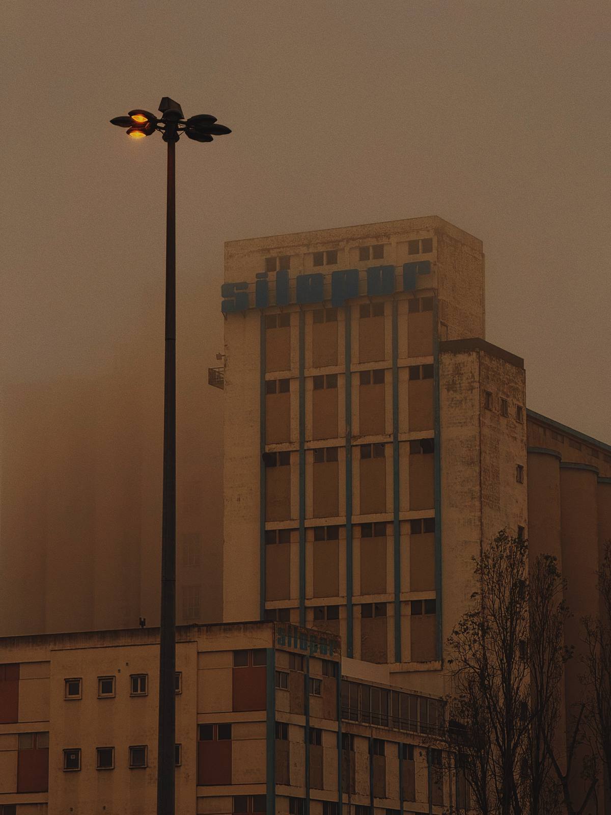 Silopor, Amber Haze, Marvila, Lisbon — Iconic Marvila grain silo dissolving into orange fog, single street lamp — the industrial east of Lisbon in one quiet, layered frame.