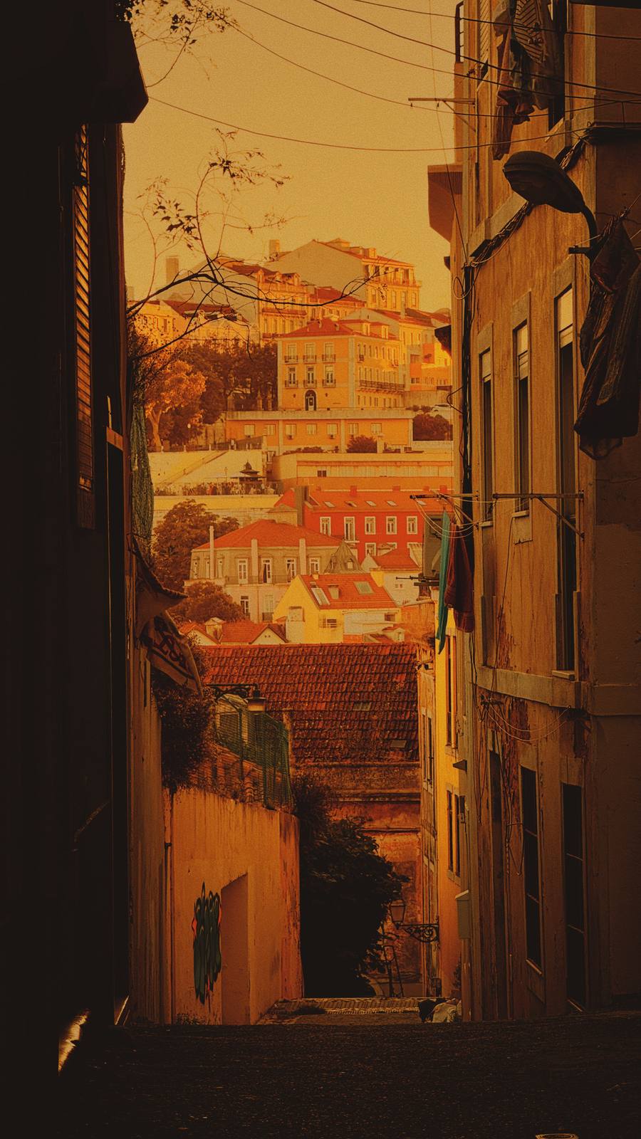 Lane Opens Onto Gold, Mouraria, Lisbon — Tight alley frame opens onto layered Lisbon rooftops bathed in deep amber — classic Mouraria depth and the brand's yellow-gold palette in full.