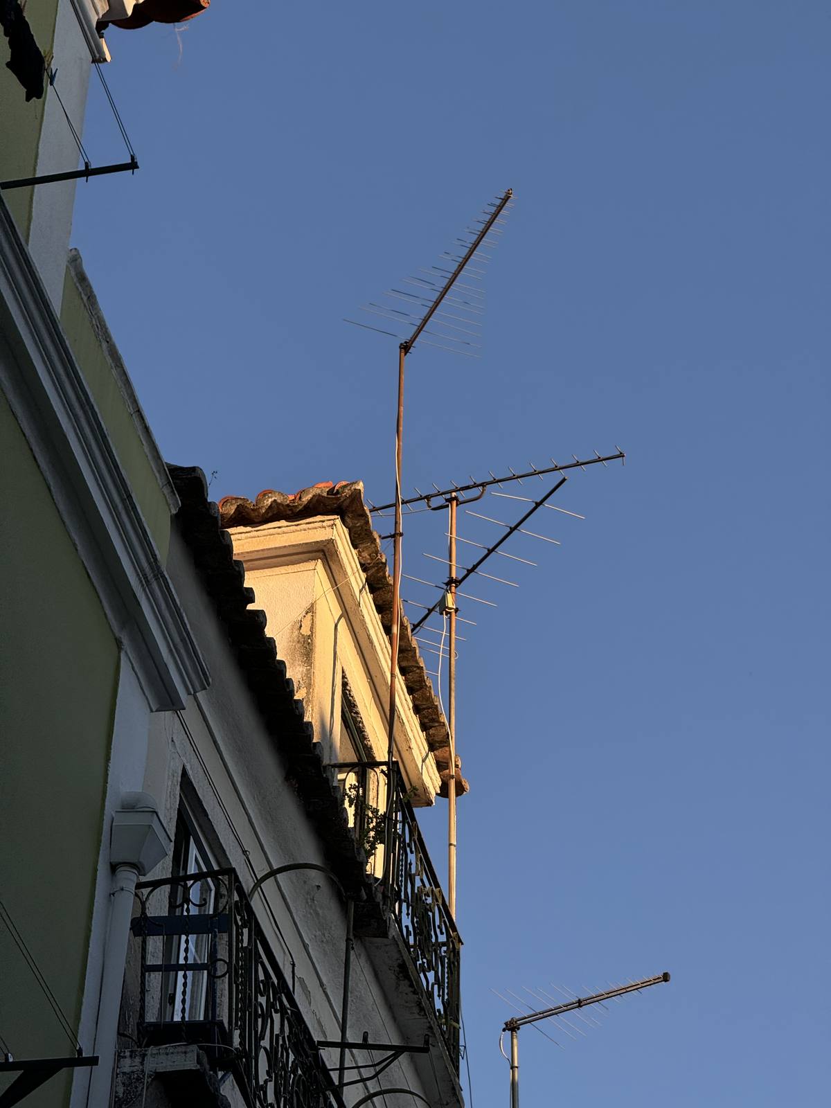 Antennas, Last Light, Mouraria, Lisbon — Spare rooftop antennas against deep blue sky with warm cornice below — quiet urban still life; compositionally minimal but reads as deliberate.