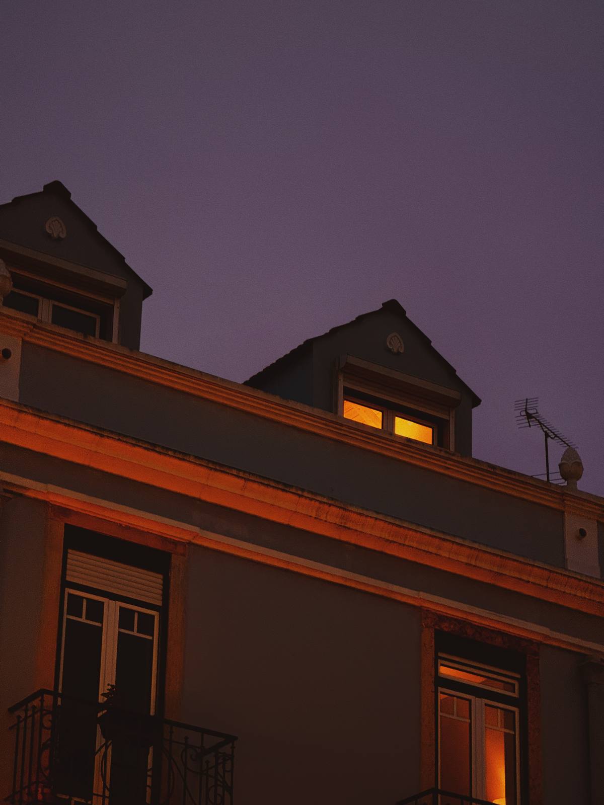One Window, Violet Hour, Penha de França, Lisbon — Single amber-lit dormer against deep violet sky — restrained, intimate, portfolio-grade quiet light.