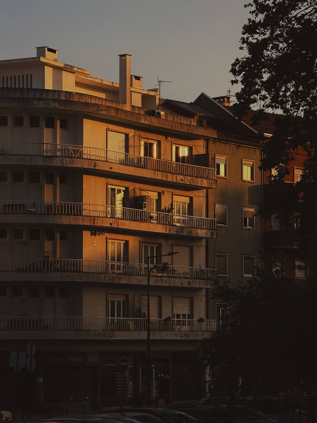 Blue Hour Balconies, Penha de França, Lisbon — A curved balcony stack caught between deep shadow and lit windows at dusk — layered warm-cool contrast, unmistakably residential Lisbon.