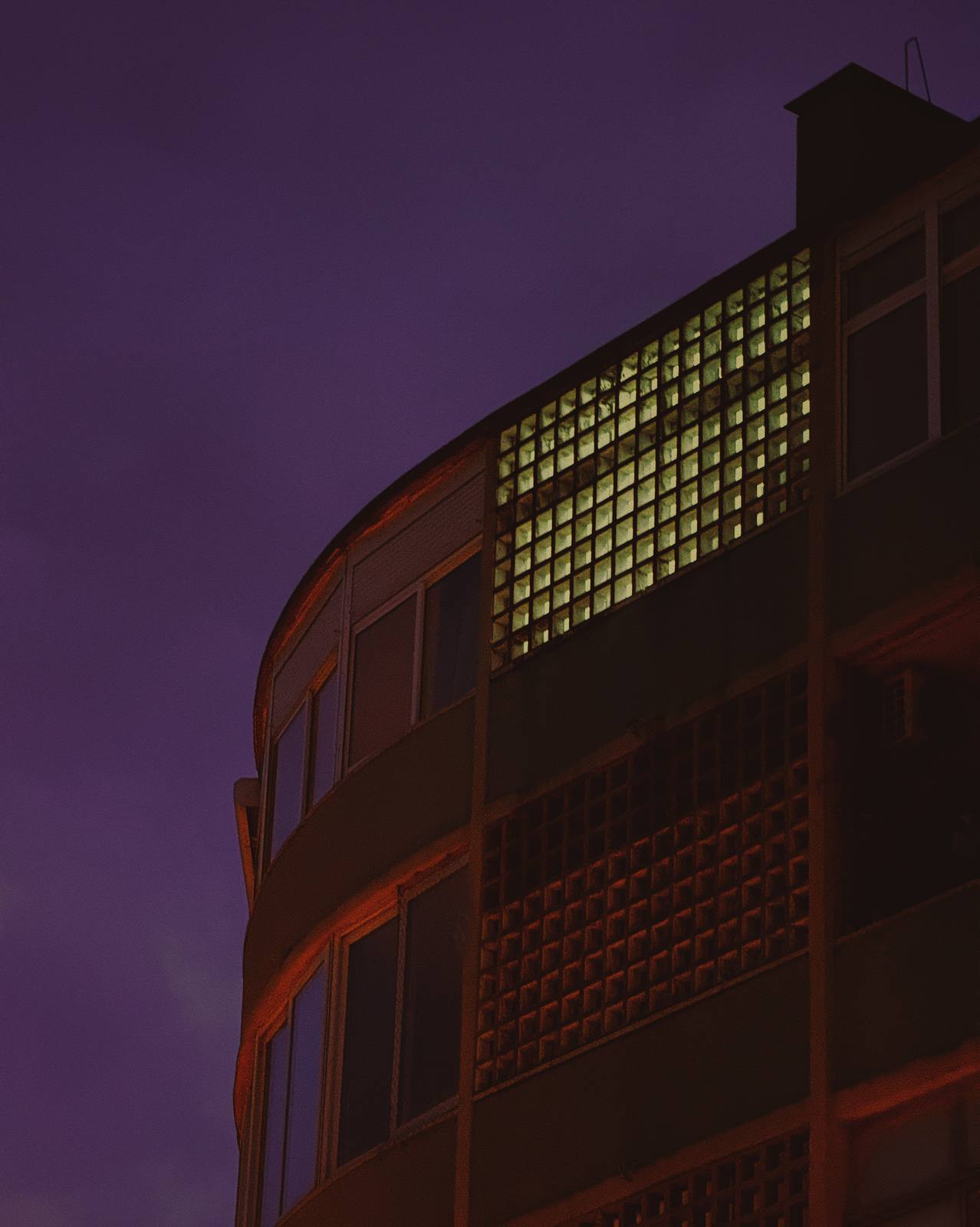 Green Grid, Purple Night, Penha de França, Lisbon — A curved modernist corner against violet sky, a single glowing green glass-block panel — singular nocturnal geometry.