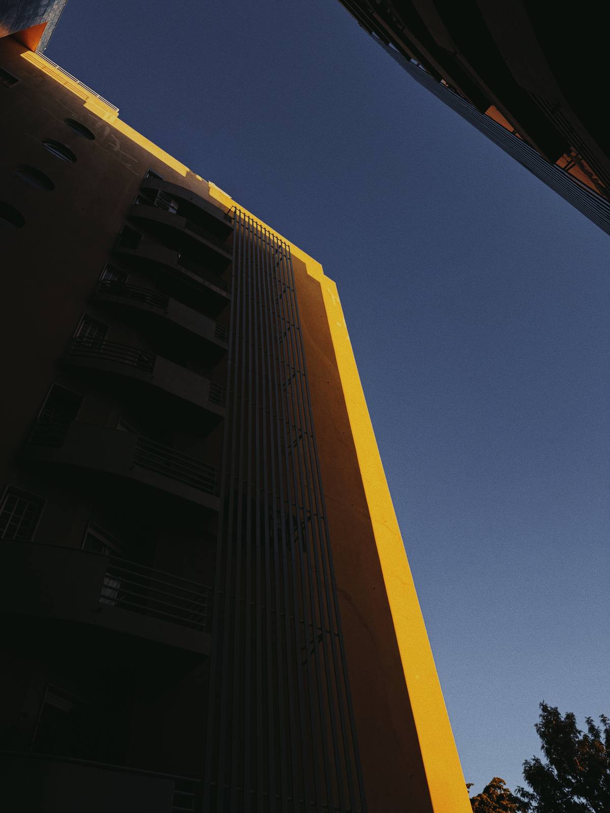 Yellow Edge Rising, Penha de França, Lisbon — Brand-yellow building edge cuts the frame against pure blue sky — graphic, bold, unmistakably ABIASSI.