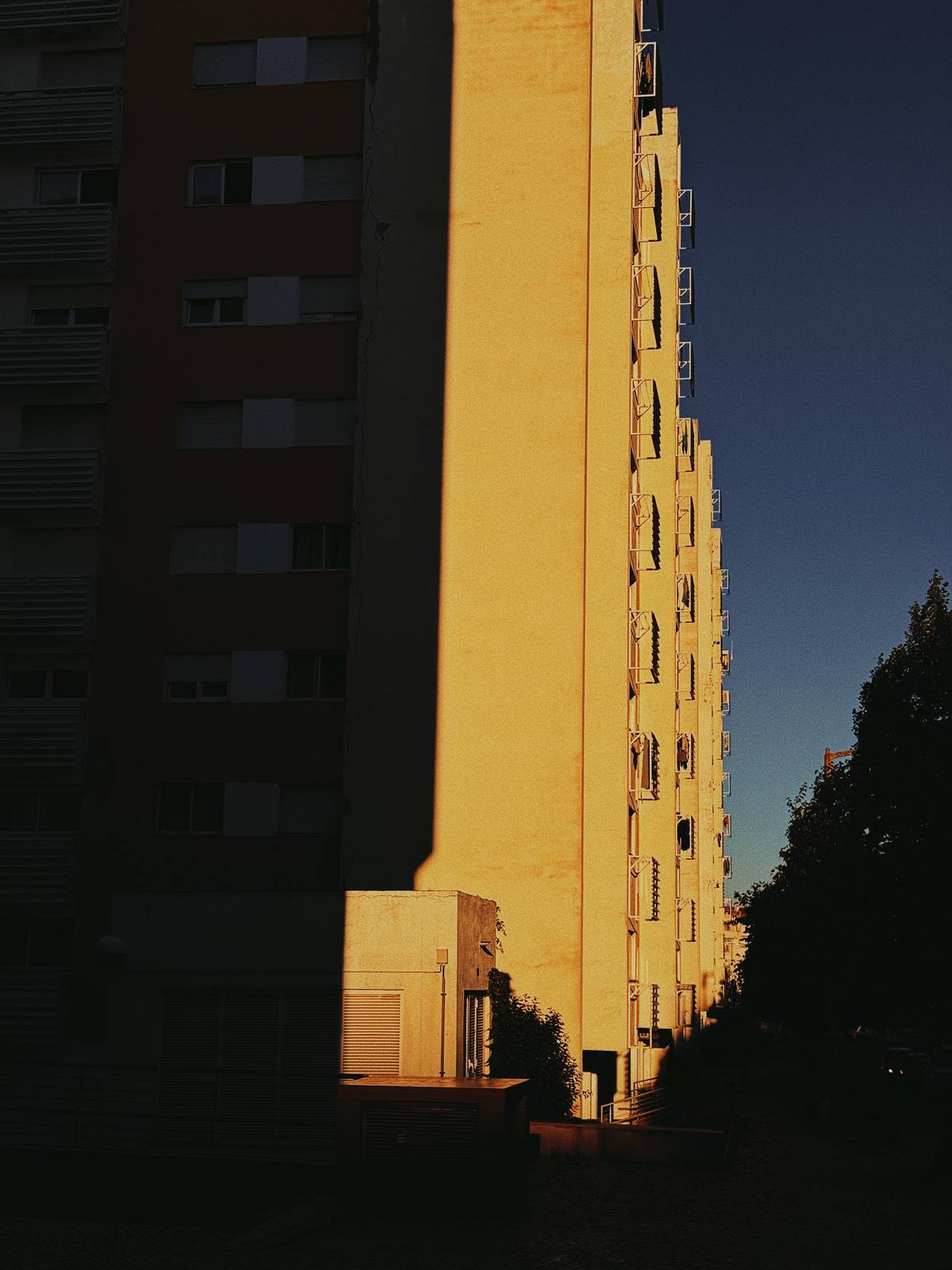Shadow Cuts the Block, Penha de França, Lisbon — Hard diagonal shadow splits the tower into deep dark and blazing amber — pure graphic tension against deep blue.