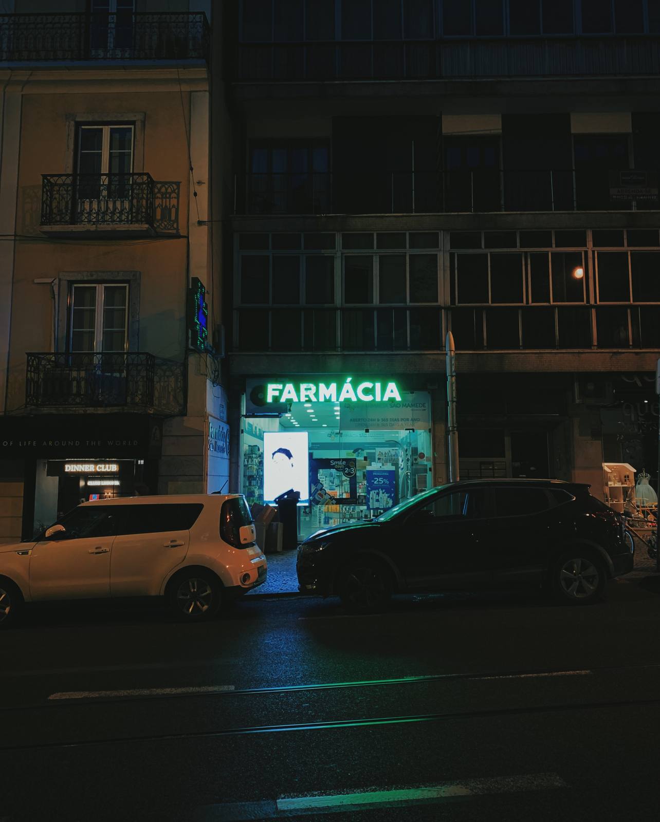 Farmácia, Green On Wet Stone, Príncipe Real, Lisbon — Properly oriented nocturnal frame: FARMÁCIA neon bleeds teal light across wet asphalt, flanked by dark parked cars and a faded Pombaline block — q